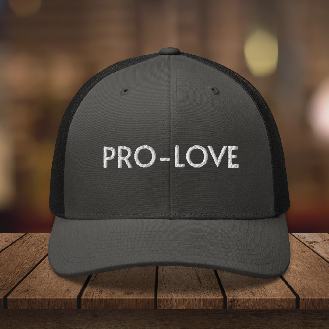 PRO-LOVE| TRUCKER HAT| FEEL THE FACTS A front view of the Pro-Love Trucker Hat, featuring the embroidered "Pro-Love" logo on the front and a stylish mesh design on the sides. BLK_CHARCOAL